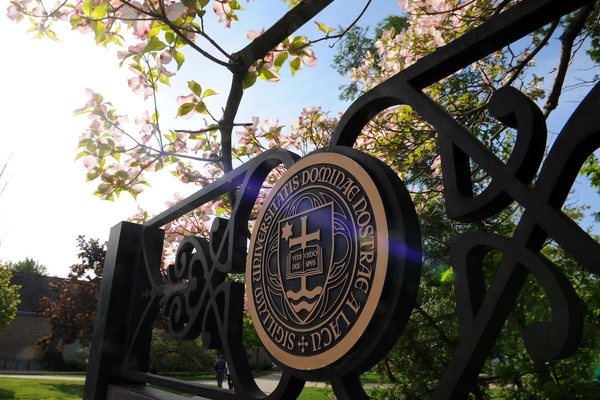 the seal of the University of Notre Dame on a campus sign with a blooming tree in the background
